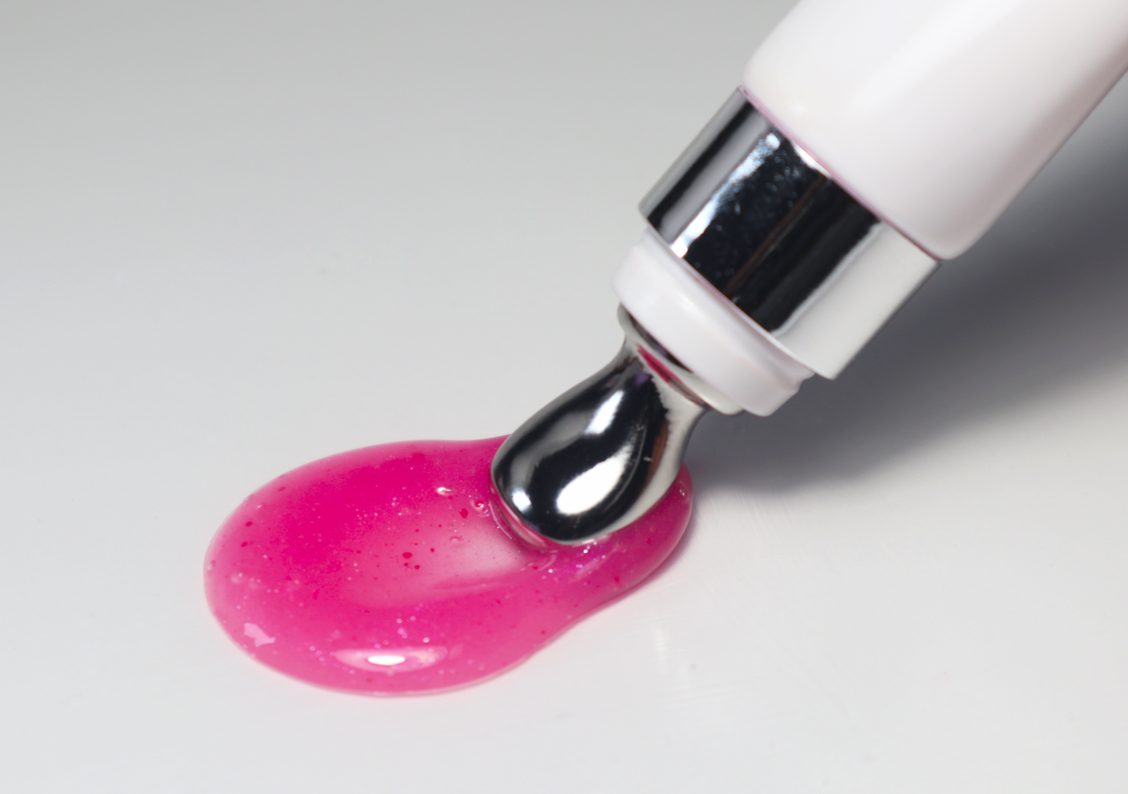 Pink gel being squeezed out of a white and silver applicator on a light gray background